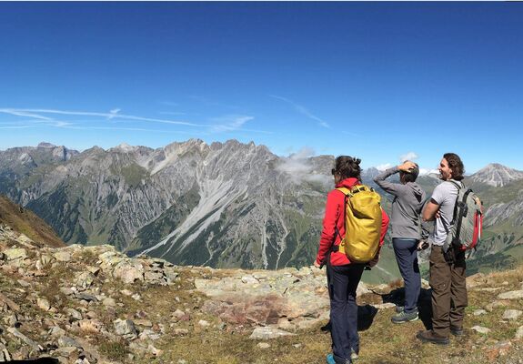 Drei Menschen bestaunen den Ausblick auf die Berge