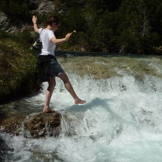 Eine junge Frau genießt das eiskalte Schmelzwasser, das in diversen Bächen die Alpen hinabstürzt