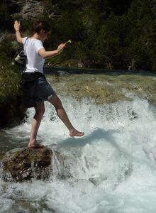 Eine junge Frau genießt das eiskalte Schmelzwasser, das in diversen Bächen die Alpen hinabstürzt