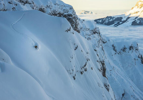 Ein Skifahrer bahnt sich seinen abenteuerlichen Weg eine Bergseite hinab durch den Tiefschnee