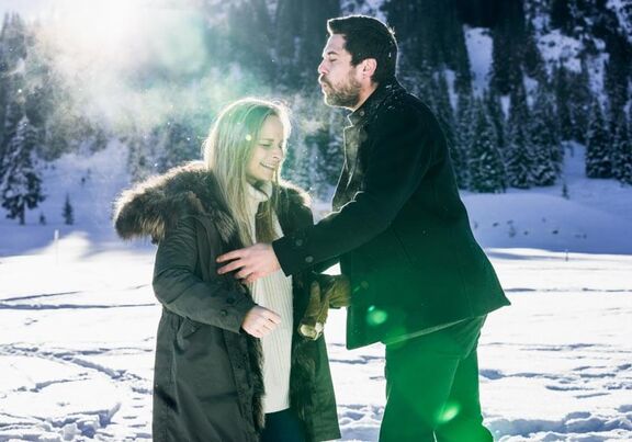 A couple is standing in the snow. Behind them a beautiful snowy landscape