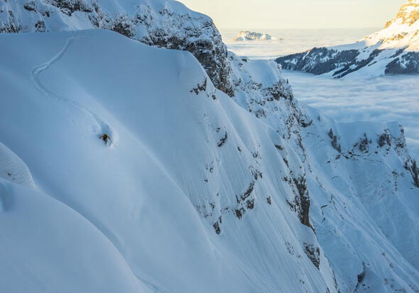 A skier makes his adventurous way down a mountain side through deep snow