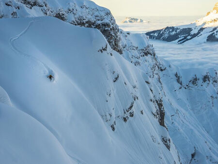 A skier makes his adventurous way down a mountain side through deep snow