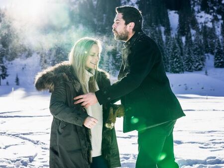 A couple is standing in the snow. Behind them a beautiful snowy landscape