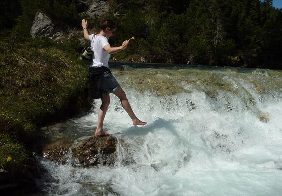 Eine junge Frau genießt das eiskalte Schmelzwasser, das in diversen Bächen die Alpen hinabstürzt