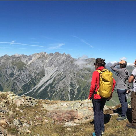 Drei Menschen bestaunen den Ausblick auf die Berge