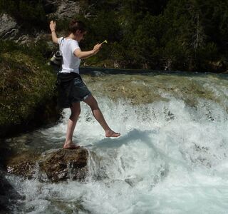 Eine junge Frau genießt das eiskalte Schmelzwasser, das in diversen Bächen die Alpen hinabstürzt